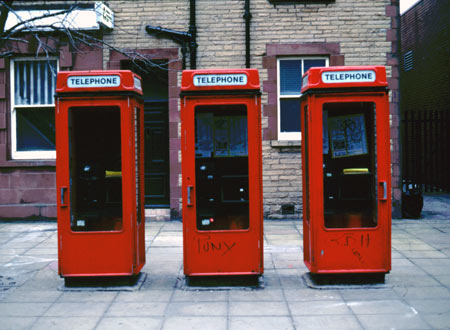 A trio of K7 telephone kiosks stand, neglected, outside 'Next'.